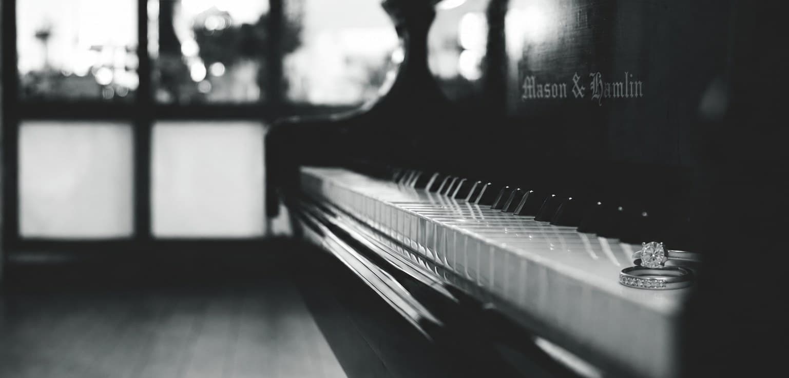Wedding rings resting on a Mason & Hamlin grand piano keyboard by an arched window